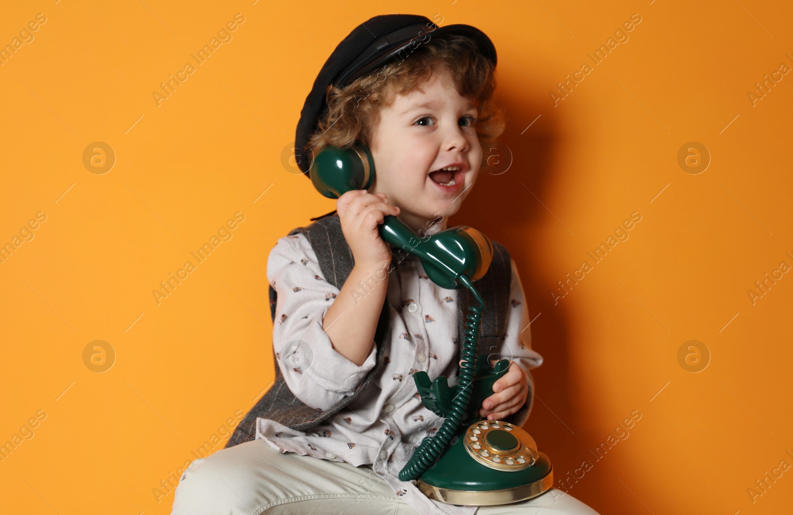 Photo of Cute little boy with old telephone on orange background