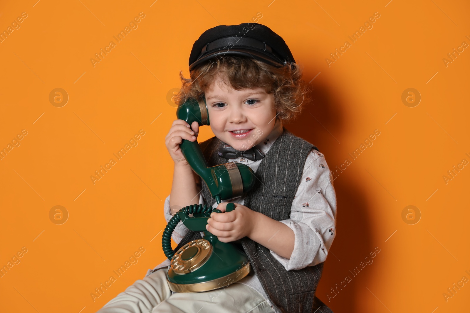 Photo of Cute little boy with old telephone on orange background