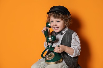 Photo of Cute little boy with old telephone on orange background, space for text