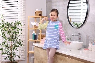 Photo of Cute girl with toothbrush on countertop in bathroom