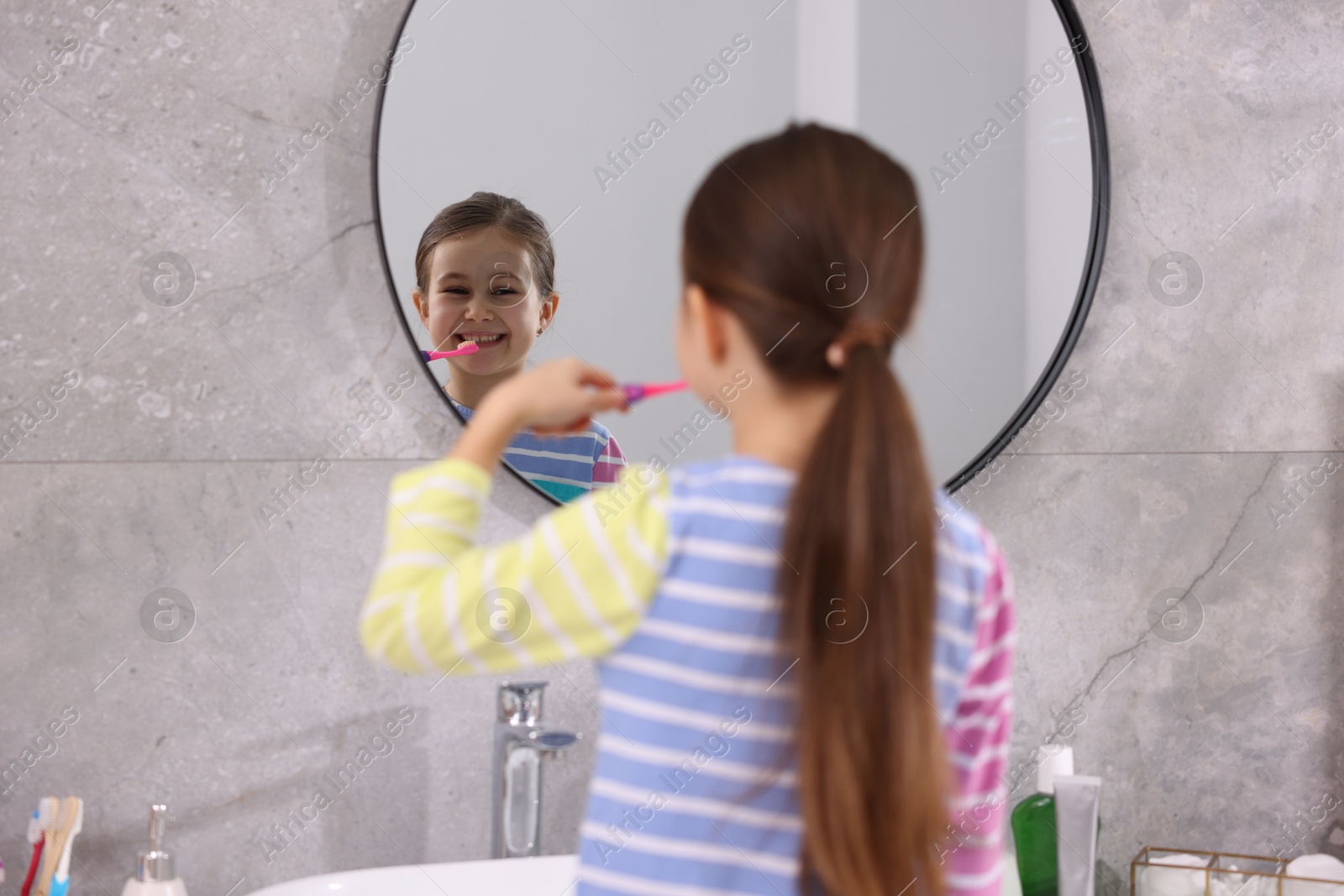 Photo of Cute girl brushing her teeth near mirror in bathroom, selective focus