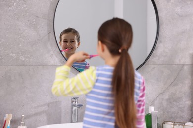 Photo of Cute girl brushing her teeth near mirror in bathroom, selective focus