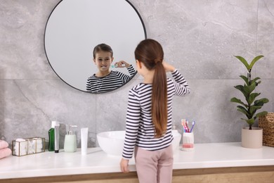 Photo of Cute girl brushing her teeth near mirror in bathroom, selective focus