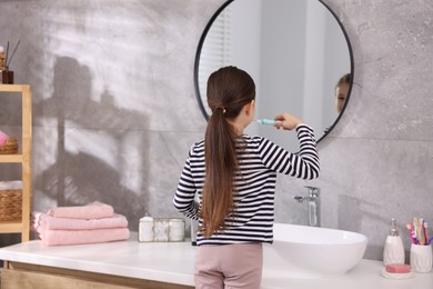 Photo of Cute girl brushing her teeth near mirror in bathroom, selective focus