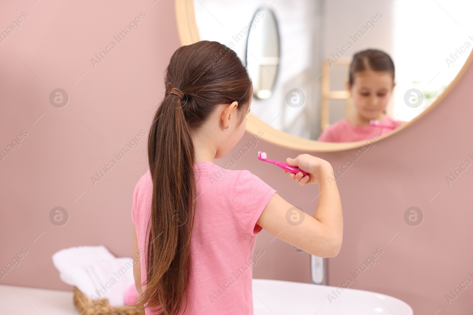 Photo of Cute girl with toothbrush near mirror in bathroom, selective focus