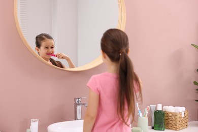 Photo of Cute girl brushing her teeth near mirror in bathroom, selective focus