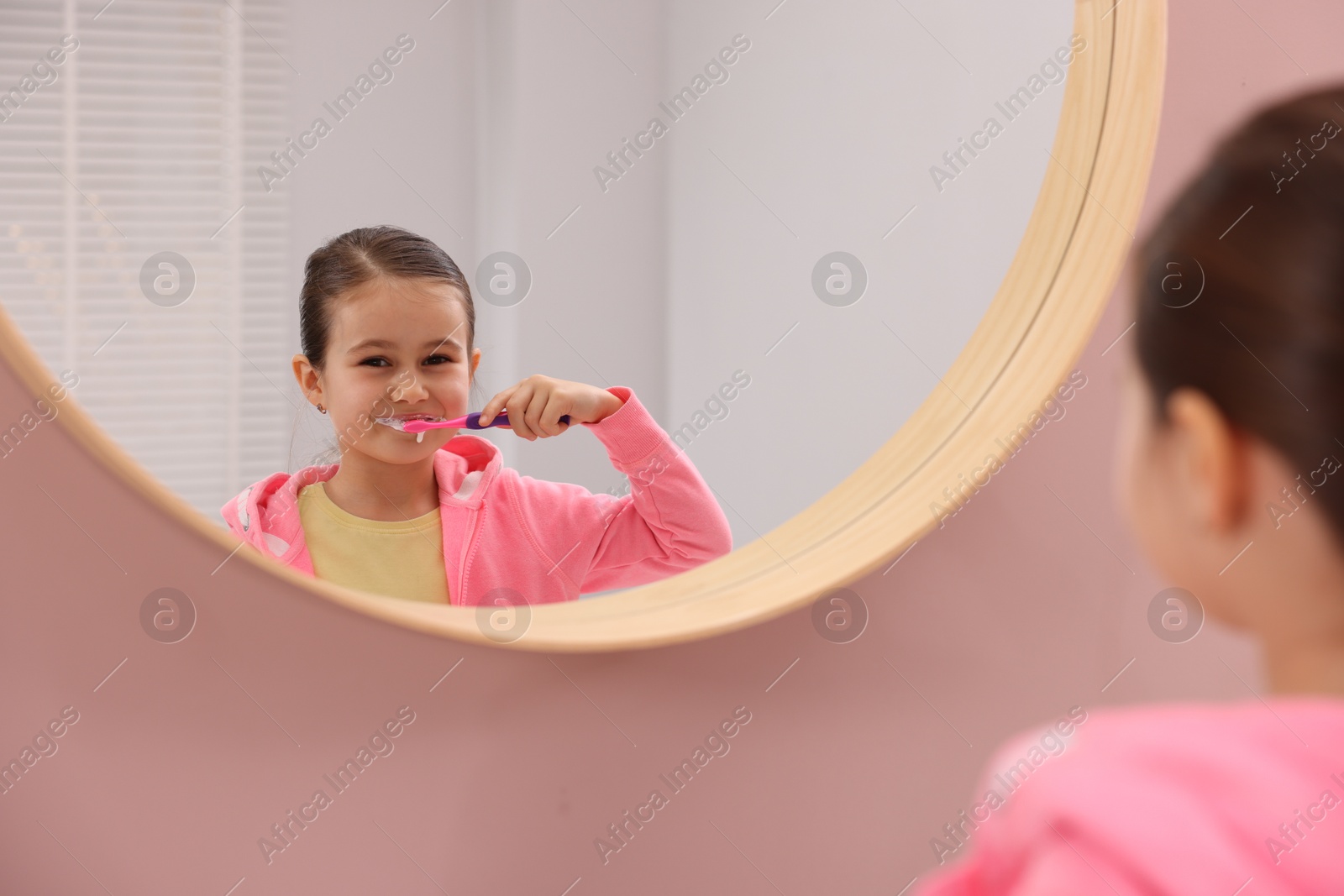 Photo of Cute girl brushing her teeth near mirror in bathroom, selective focus