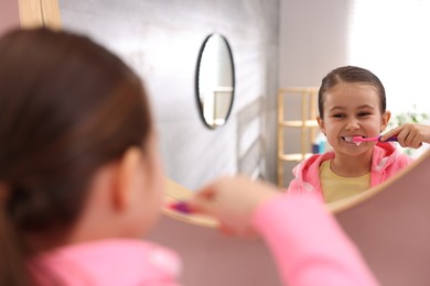 Photo of Cute girl brushing her teeth near mirror in bathroom, selective focus