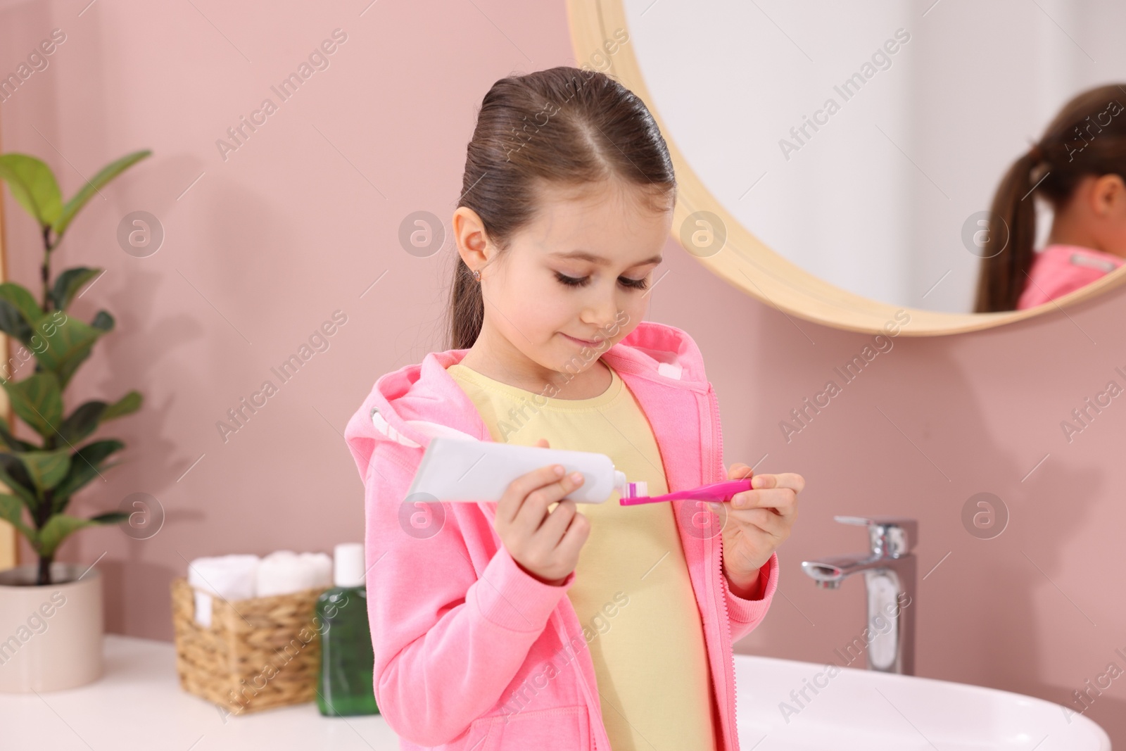 Photo of Cute girl applying toothpaste onto toothbrush in bathroom