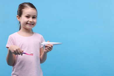 Photo of Cute girl with toothbrush and tube of toothpaste on light blue background, space for text