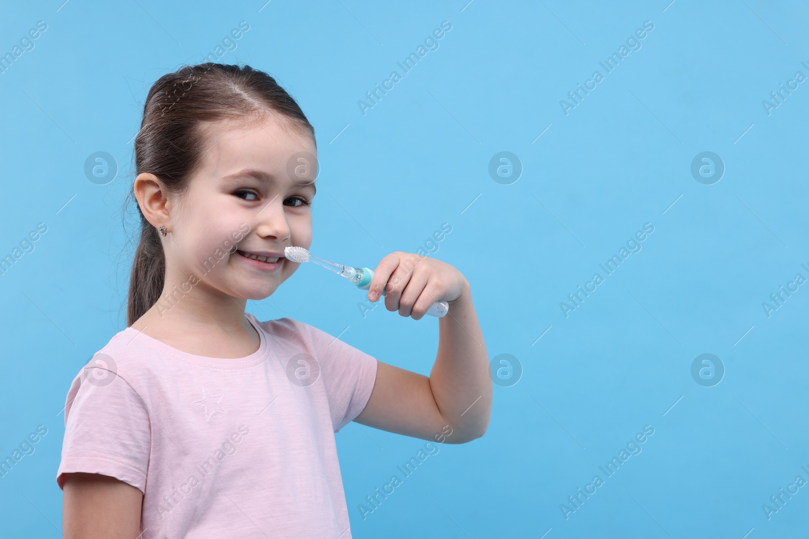 Photo of Cute girl brushing her teeth on light blue background, space for text