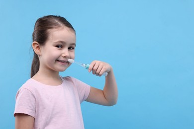 Photo of Cute girl brushing her teeth on light blue background, space for text