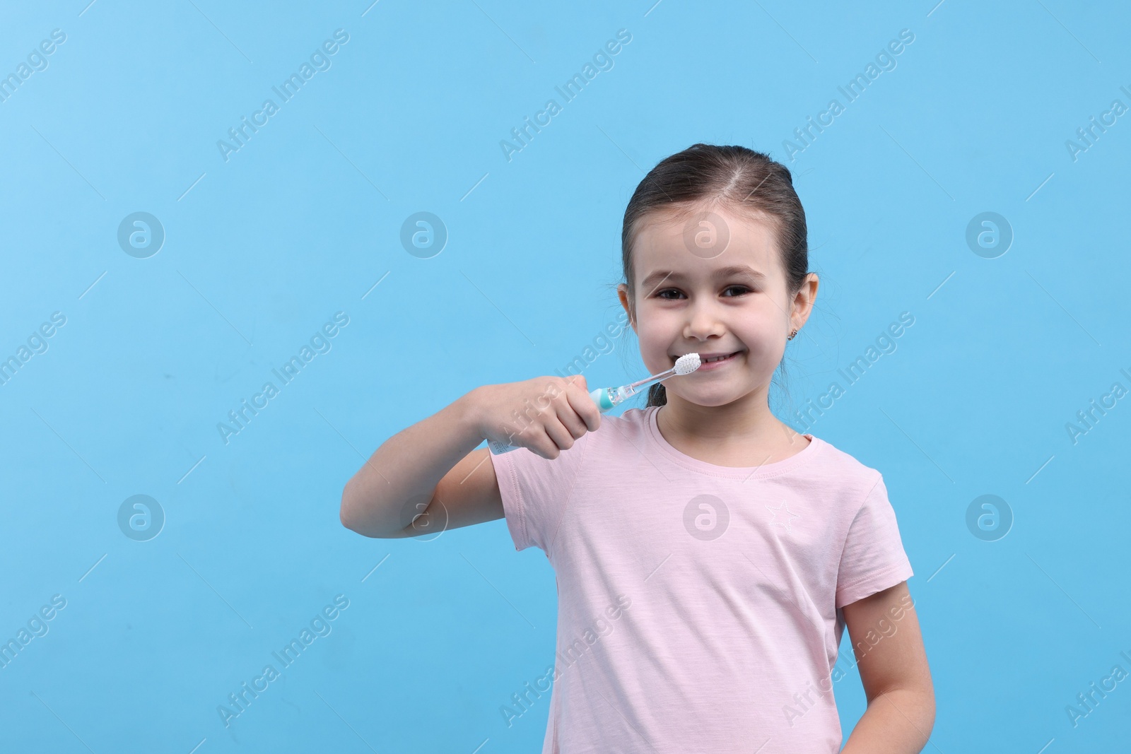 Photo of Cute girl brushing her teeth on light blue background, space for text