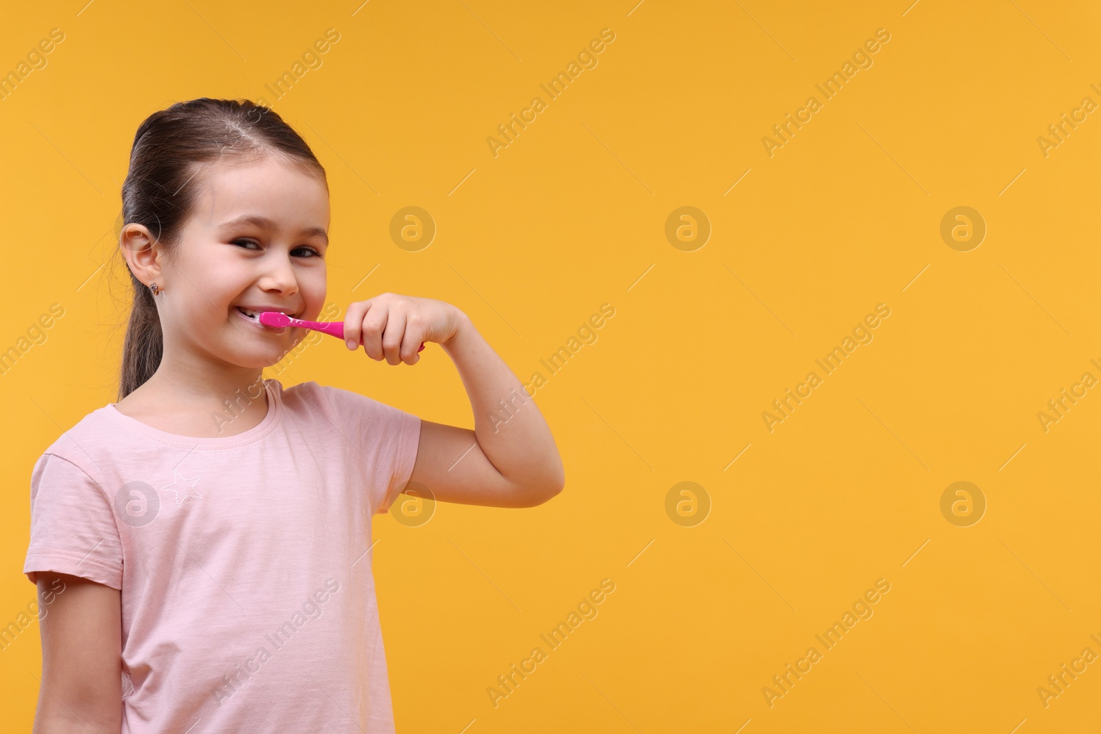 Photo of Cute girl brushing her teeth on orange background, space for text