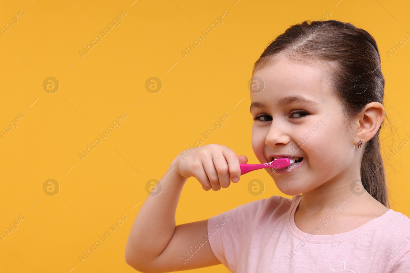 Photo of Cute girl brushing her teeth on orange background, space for text