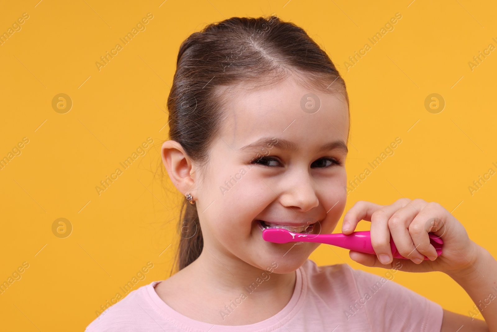 Photo of Cute girl brushing her teeth on orange background