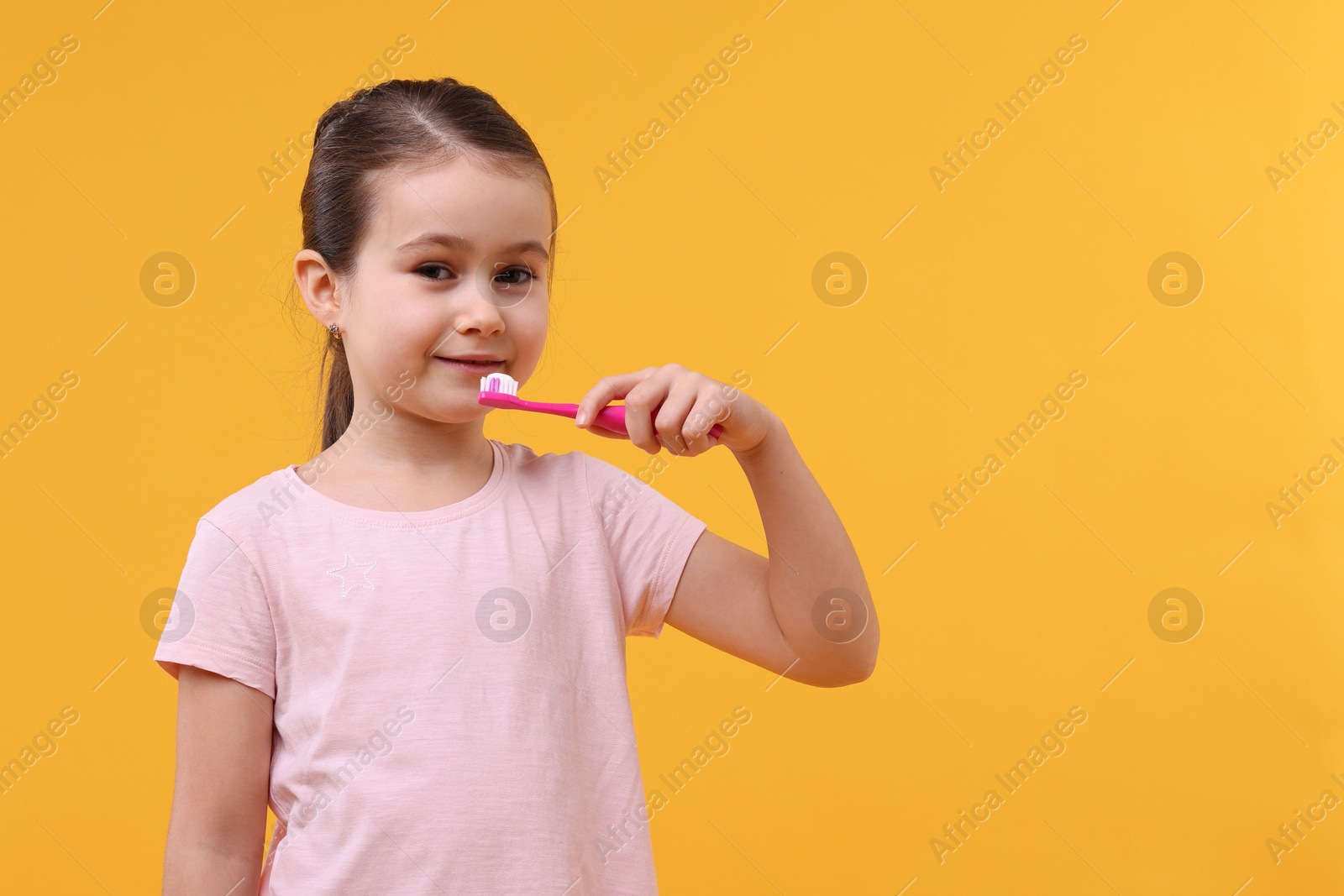 Photo of Cute girl brushing her teeth on orange background, space for text