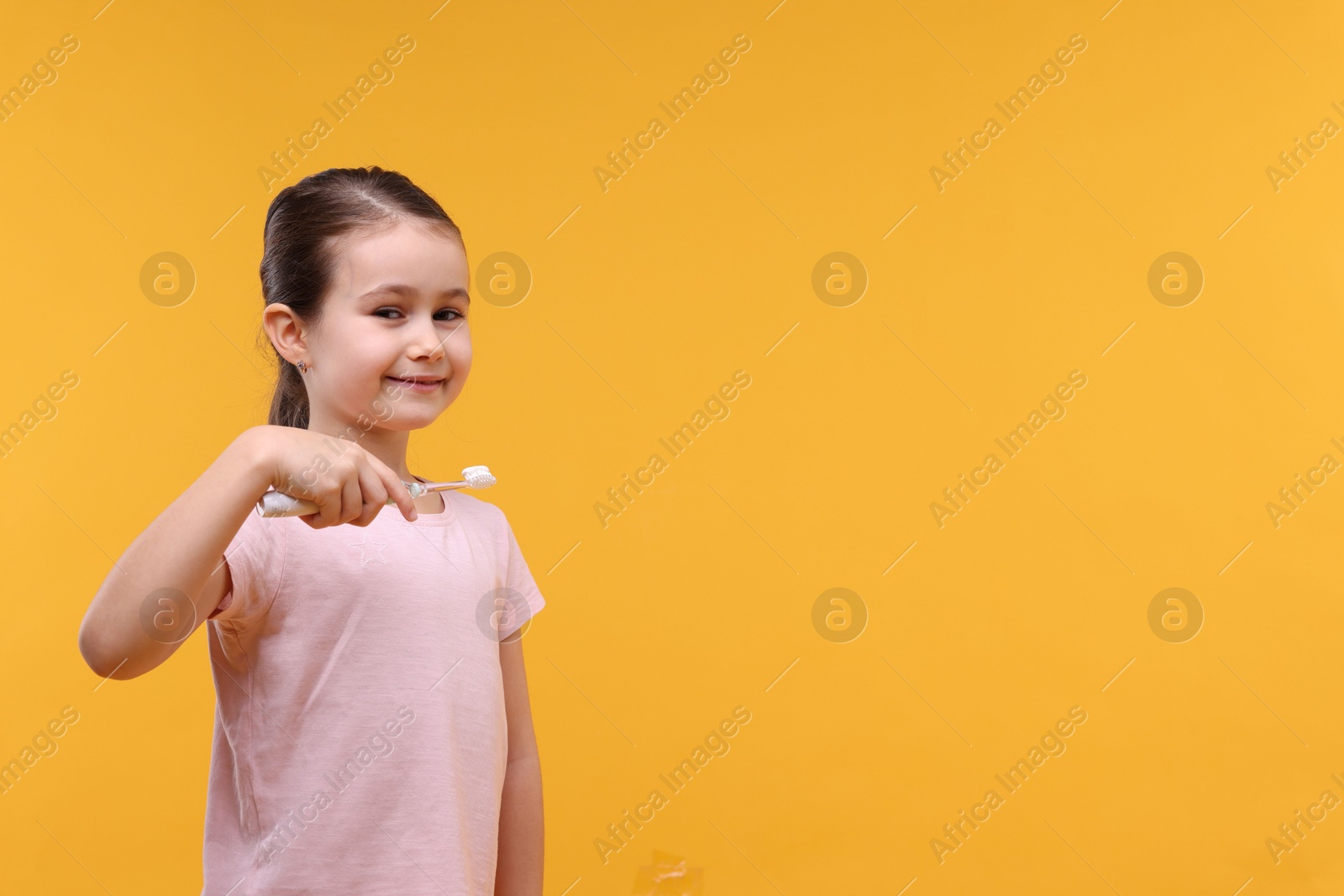 Photo of Cute girl with toothbrush on orange background, space for text