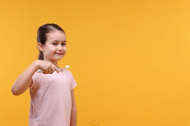 Photo of Cute girl with toothbrush on orange background, space for text