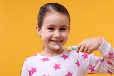 Photo of Cute girl with toothbrush on orange background