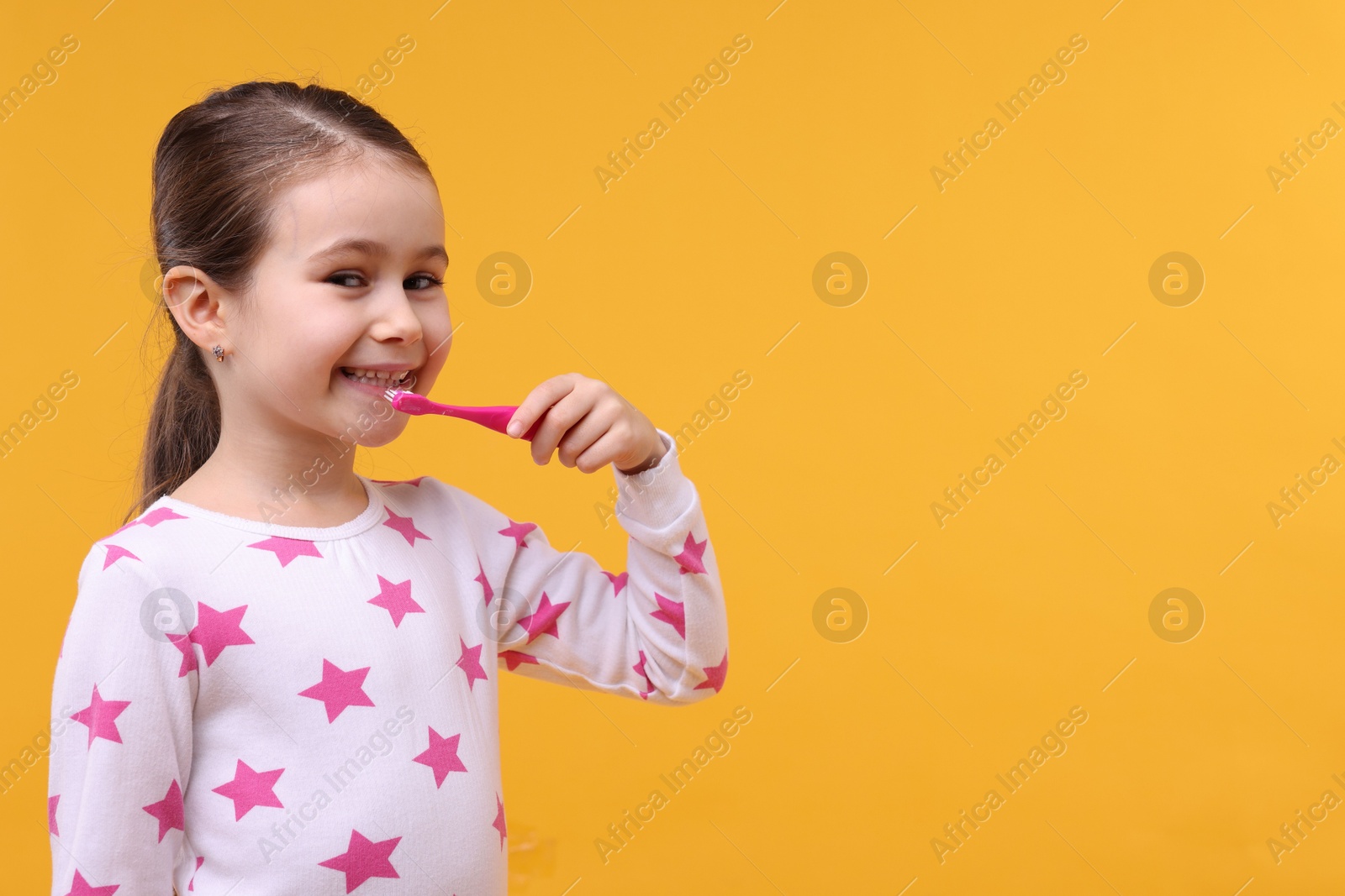 Photo of Cute girl brushing her teeth on orange background, space for text