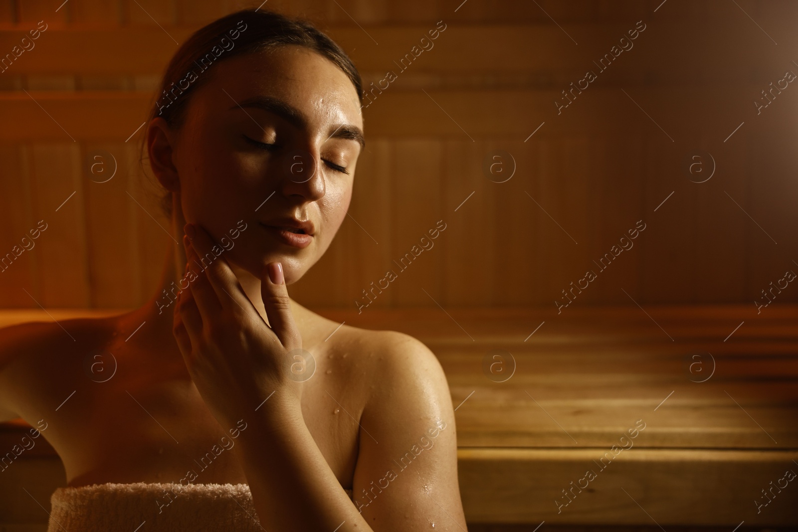 Photo of Beautiful woman wrapped in towel on bench at sauna. Space for text