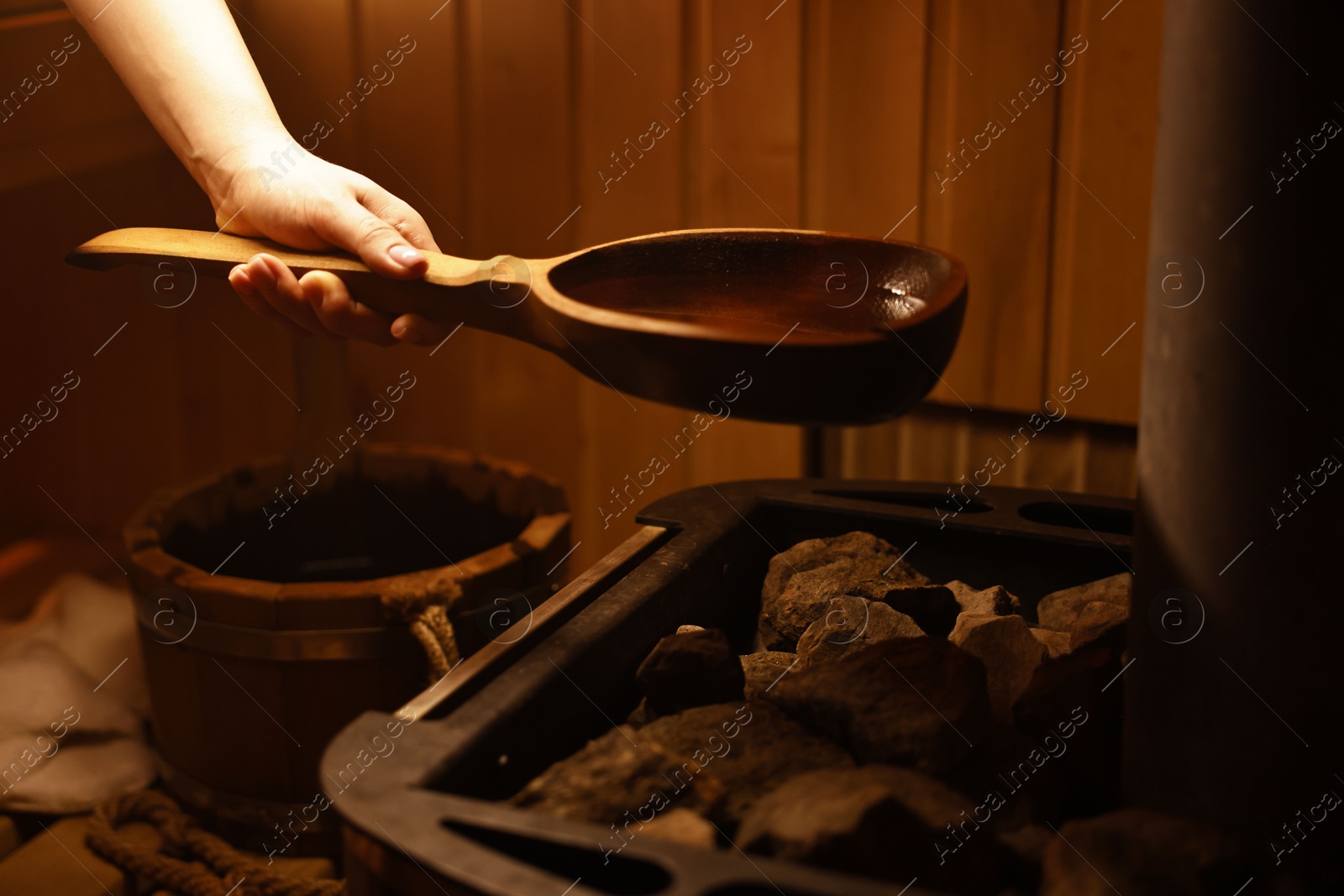 Photo of Woman pouring water on stones in sauna, closeup