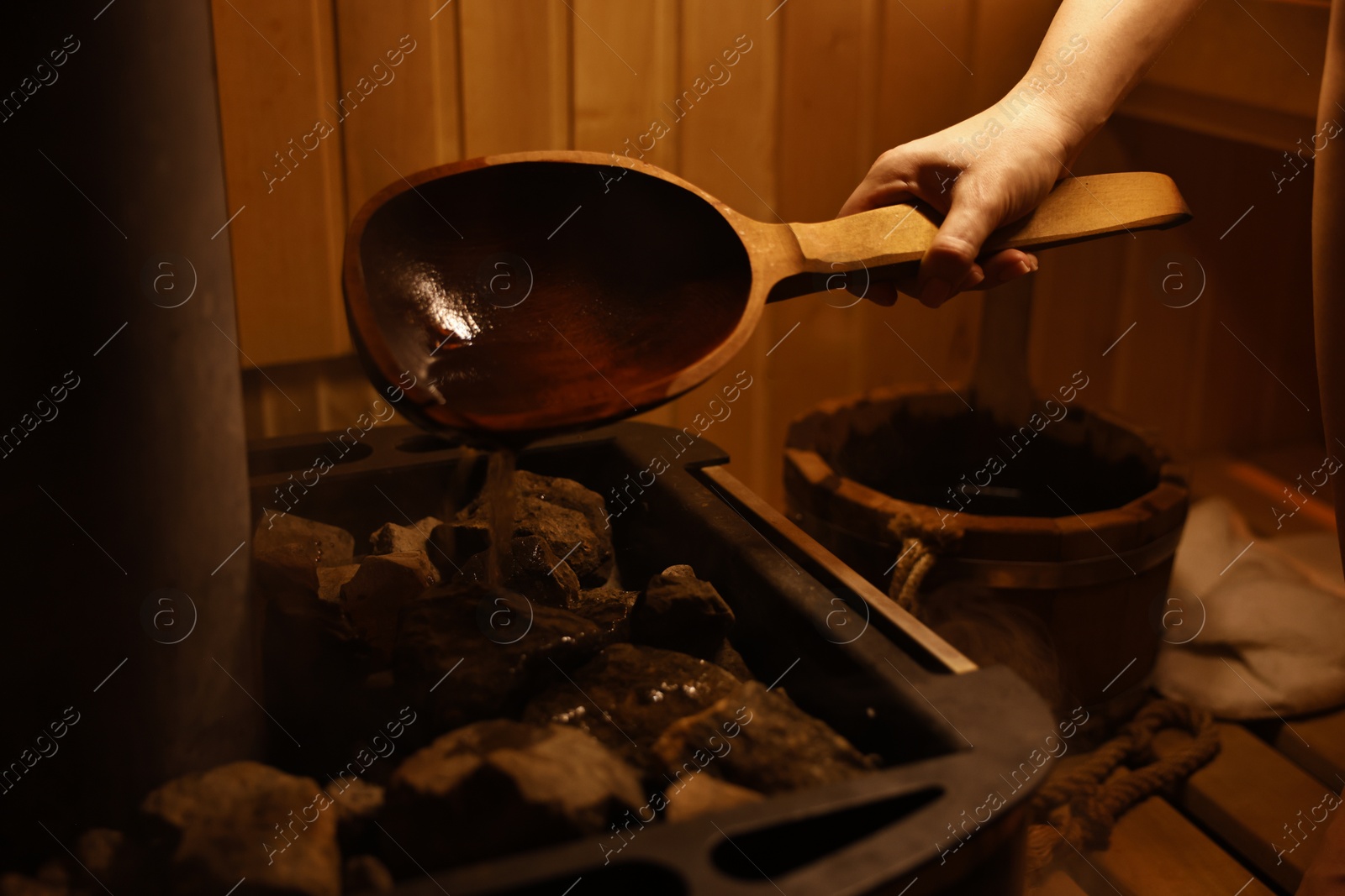 Photo of Woman pouring water on stones in sauna, closeup