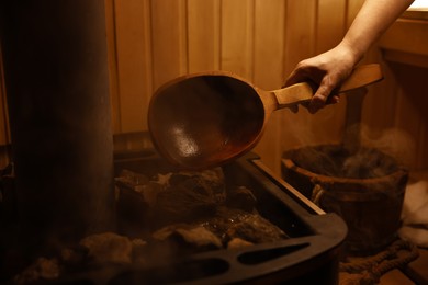 Photo of Woman pouring water on stones in sauna, closeup