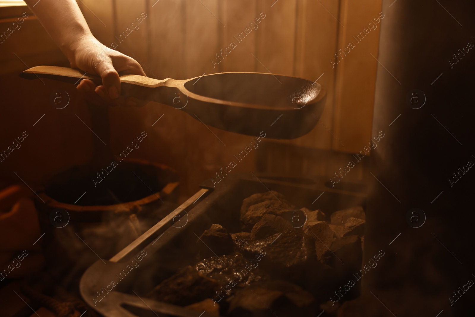 Photo of Woman pouring water on stones in sauna, closeup