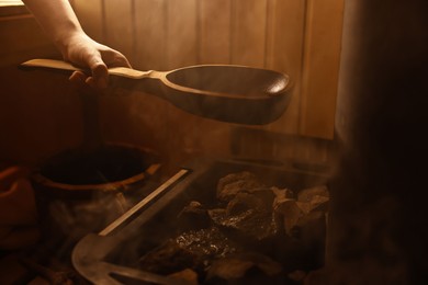 Photo of Woman pouring water on stones in sauna, closeup