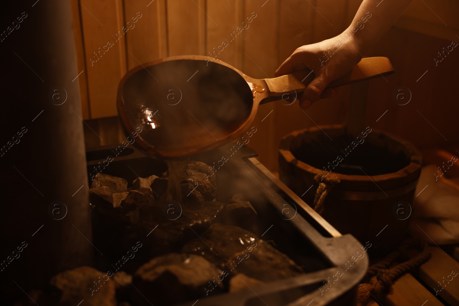 Photo of Woman pouring water on stones in sauna, closeup