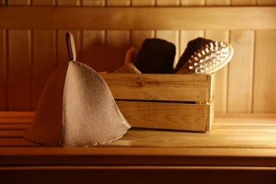 Photo of Crate with bath accessories and felt wool hat on wooden bench in sauna