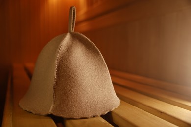 Photo of Felt wool hat on wooden bench in sauna, closeup. Space for text