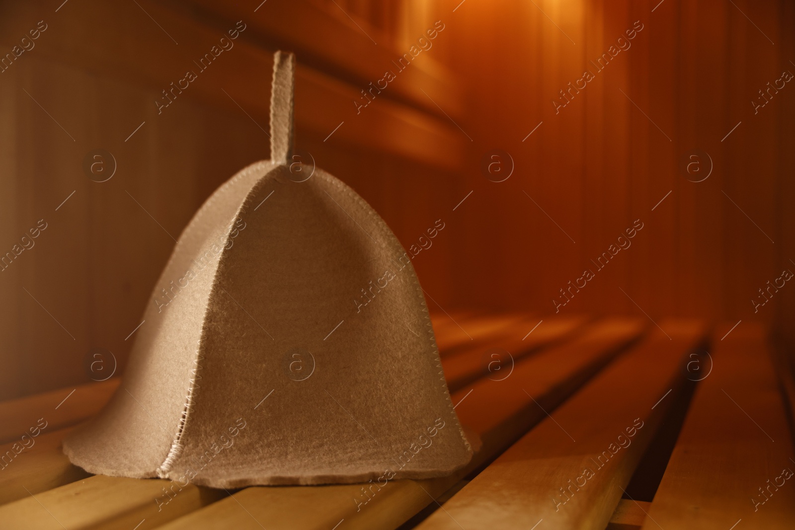 Photo of Felt wool hat on wooden bench in sauna, closeup. Space for text