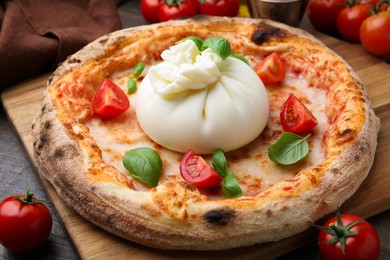 Photo of Delicious pizza with burrata cheese, basil and tomatoes on table, closeup