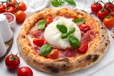 Photo of Delicious pizza with burrata cheese, basil, tomatoes and ham on table, closeup