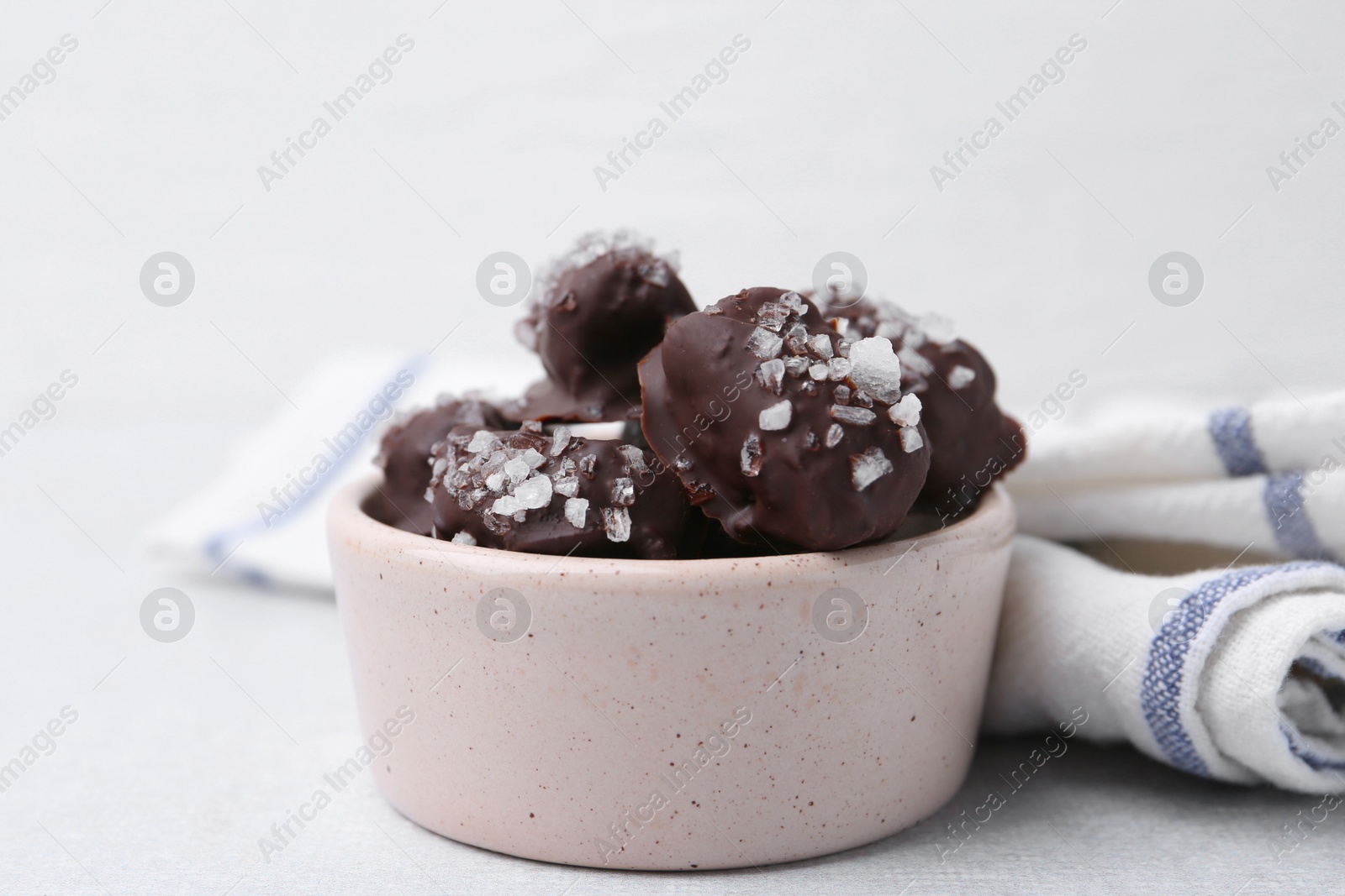 Photo of Tasty chocolate candies with salt in bowl on light table, closeup