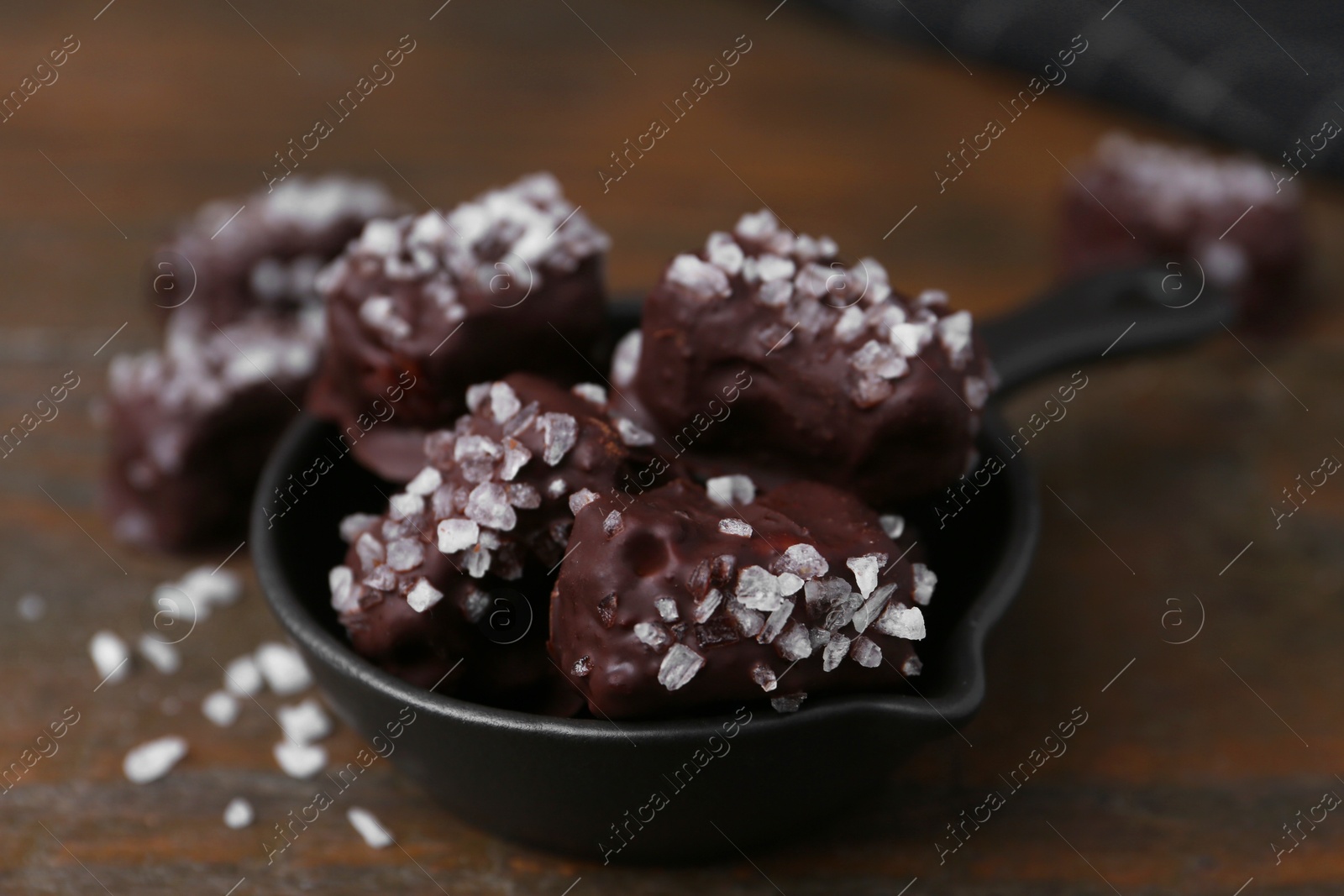 Photo of Tasty chocolate candies with salt in bowl on wooden table, closeup