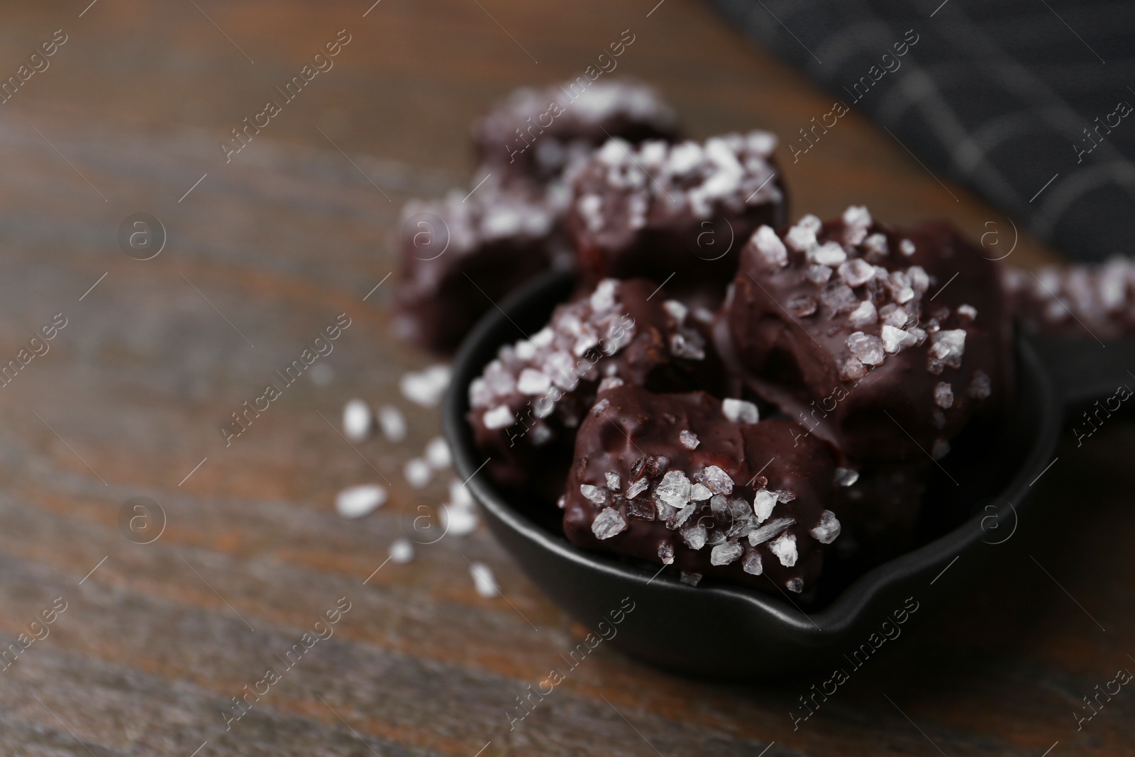 Photo of Tasty chocolate candies with salt in bowl on wooden table, closeup. Space for text