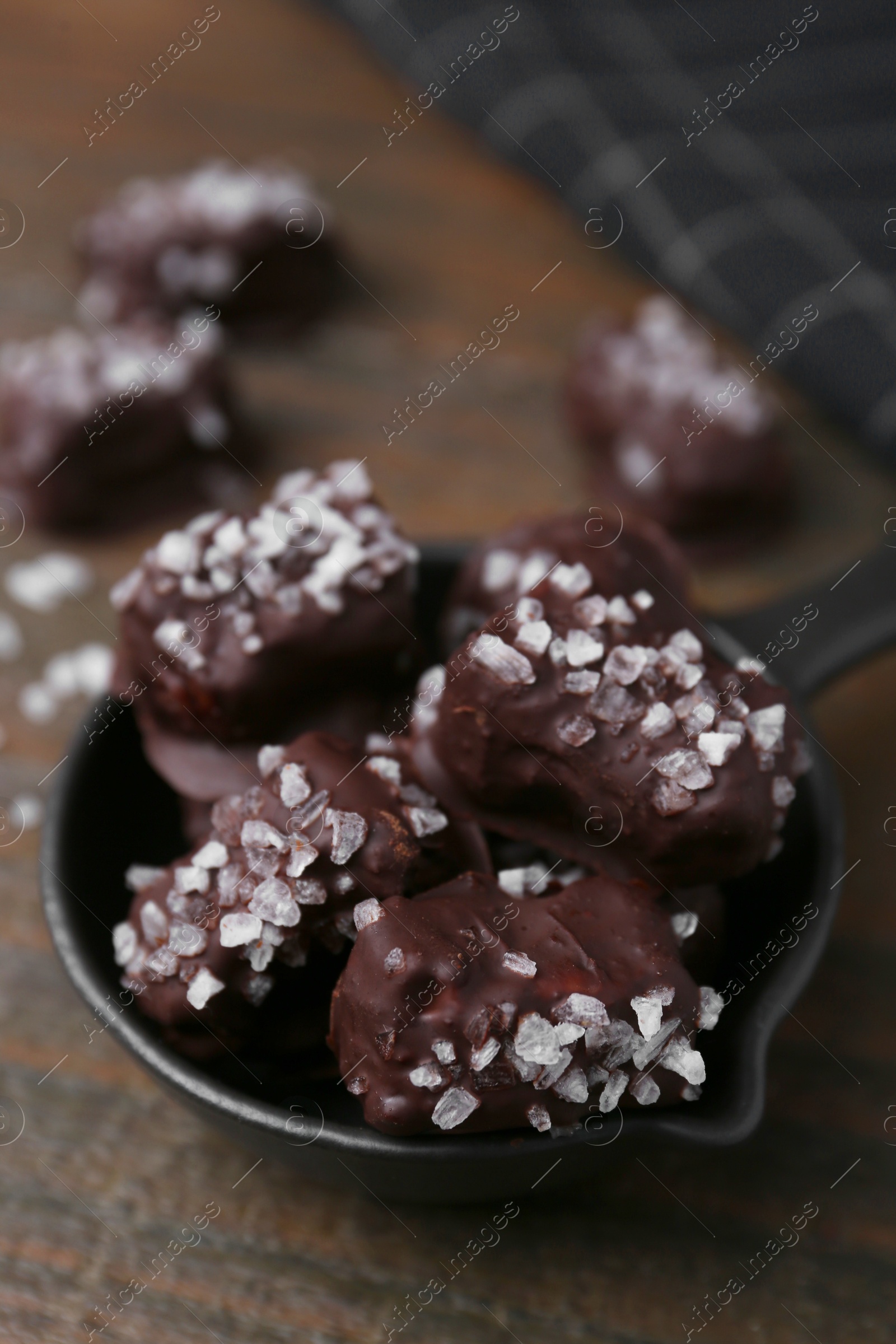 Photo of Tasty chocolate candies with salt in bowl on wooden table, closeup