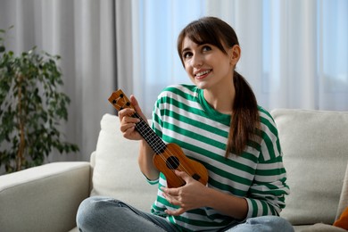 Photo of Happy woman playing ukulele on sofa at home