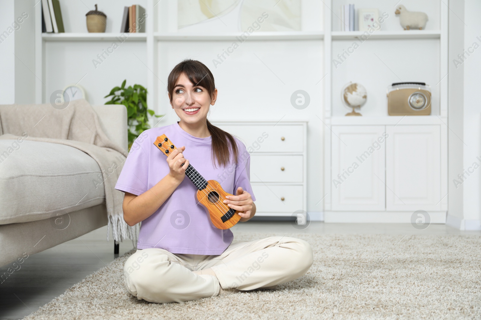 Photo of Happy woman playing ukulele on floor at home, space for text