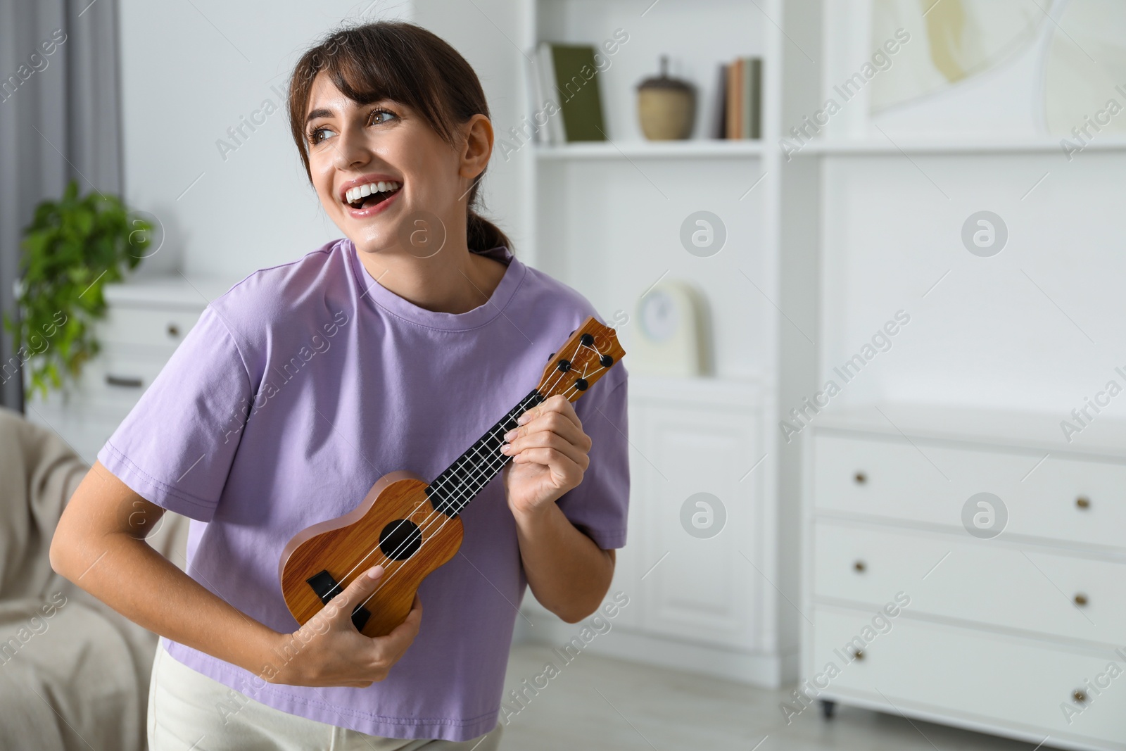 Photo of Happy woman playing ukulele at home, space for text