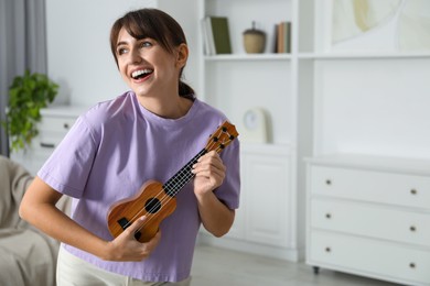 Photo of Happy woman playing ukulele at home, space for text