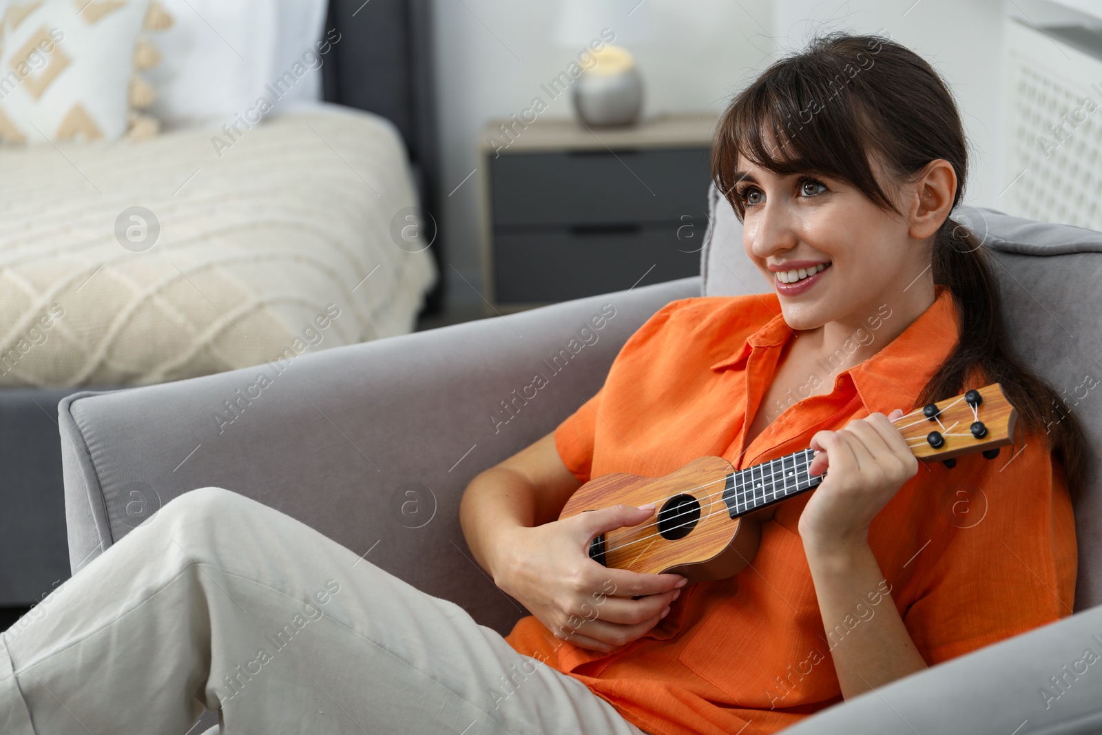 Photo of Happy woman playing ukulele in armchair at home