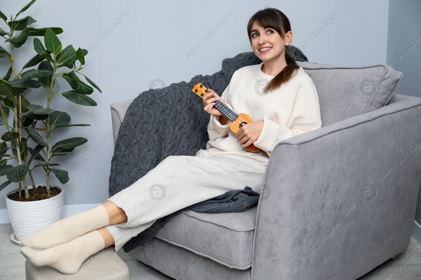 Photo of Happy woman playing ukulele in armchair at home