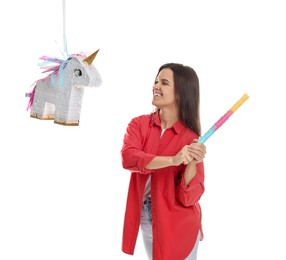 Happy woman hitting unicorn shaped pinata with stick on white background