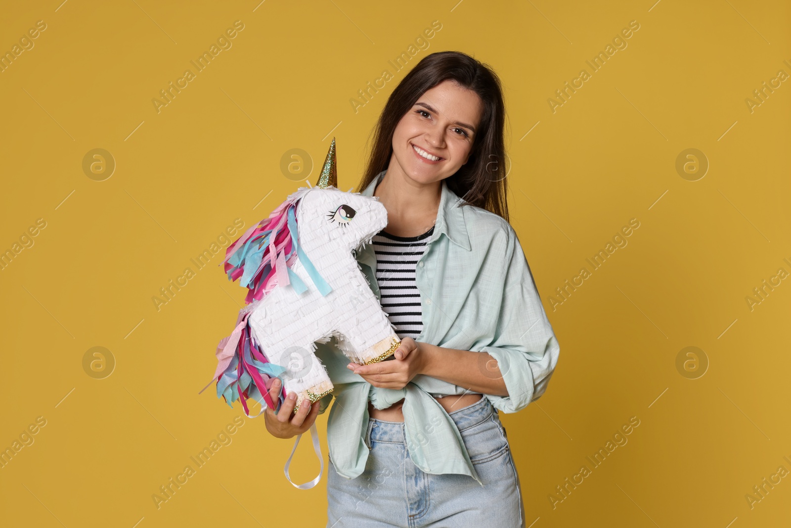 Photo of Happy woman with unicorn shaped pinata on yellow background