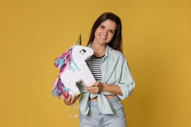 Photo of Happy woman with unicorn shaped pinata on yellow background